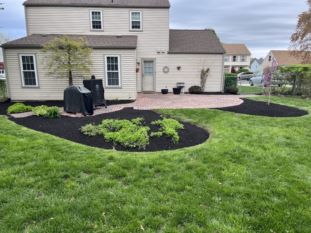 Colonial backyard with fresh mulch beds and brick patio wide view landscaping