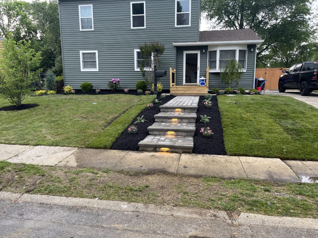Gray house front yard with paver steps and landscape lighting at dusk