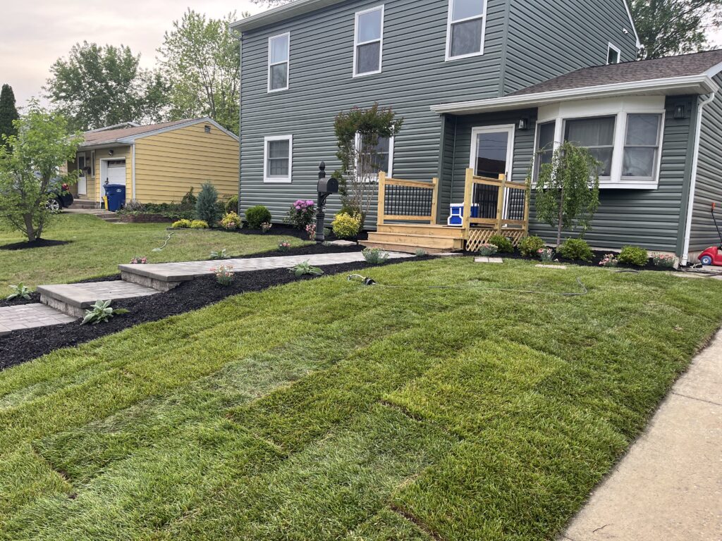 Gray house front yard with new sod installation and paver steps street view