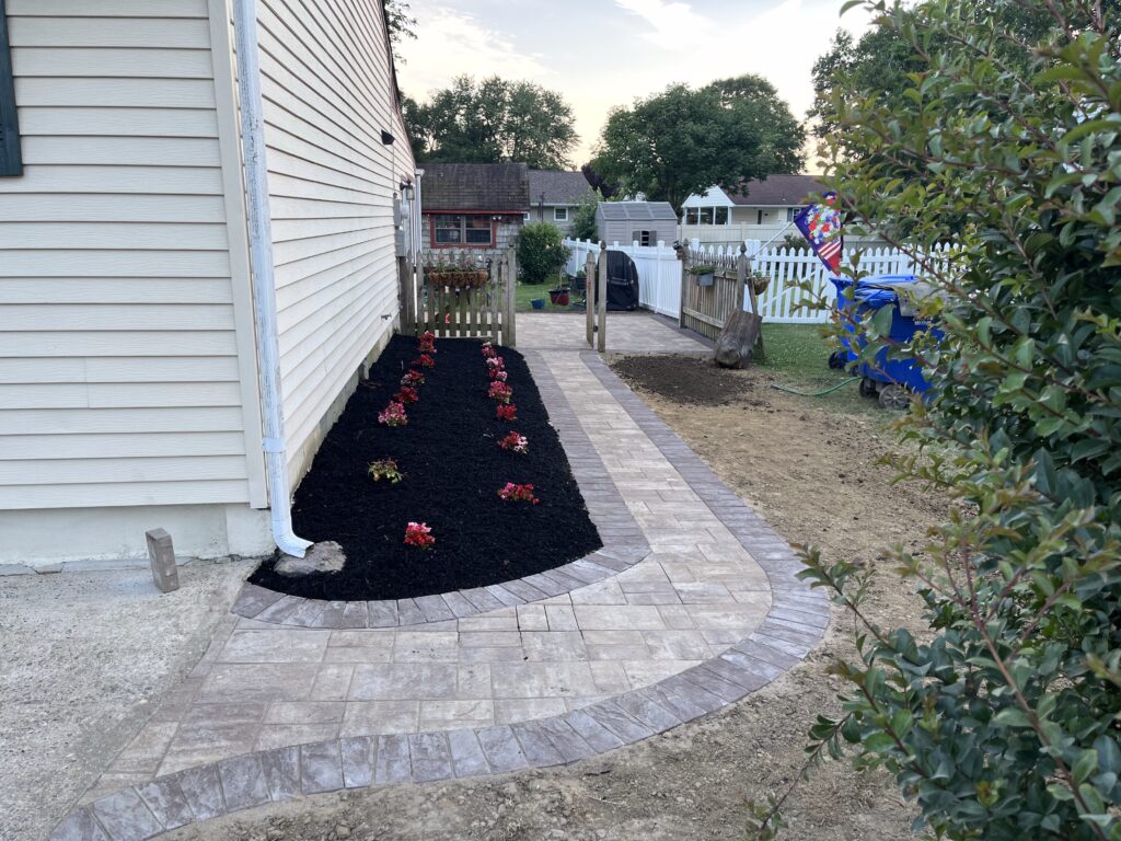 Side yard paver pathway installation with new mulch bed and red flower plantings