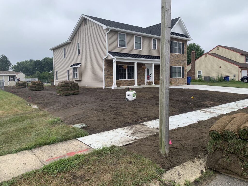 Front yard soil preparation with sod pallets staged before installation on stone facade home