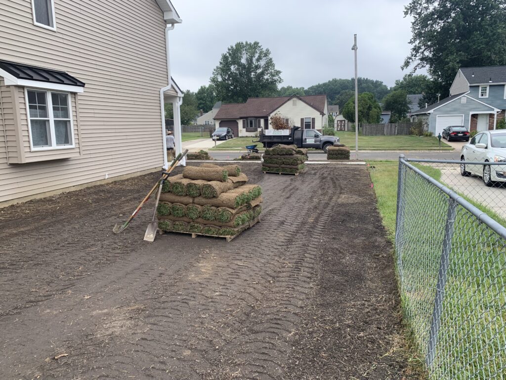 Sod pallets staged on side yard before installation at stone facade home
